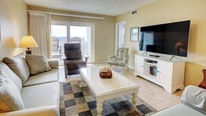 A living room with a sofa, armchair, coffee table, TV, and a balcony view. - El Matador 268 -  FREE TICKETS!! Your stay includes free tickets to many area attractions! (Fort Walton Beach)