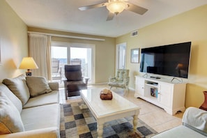 A living room with a sofa, armchair, coffee table, TV, and a balcony view.