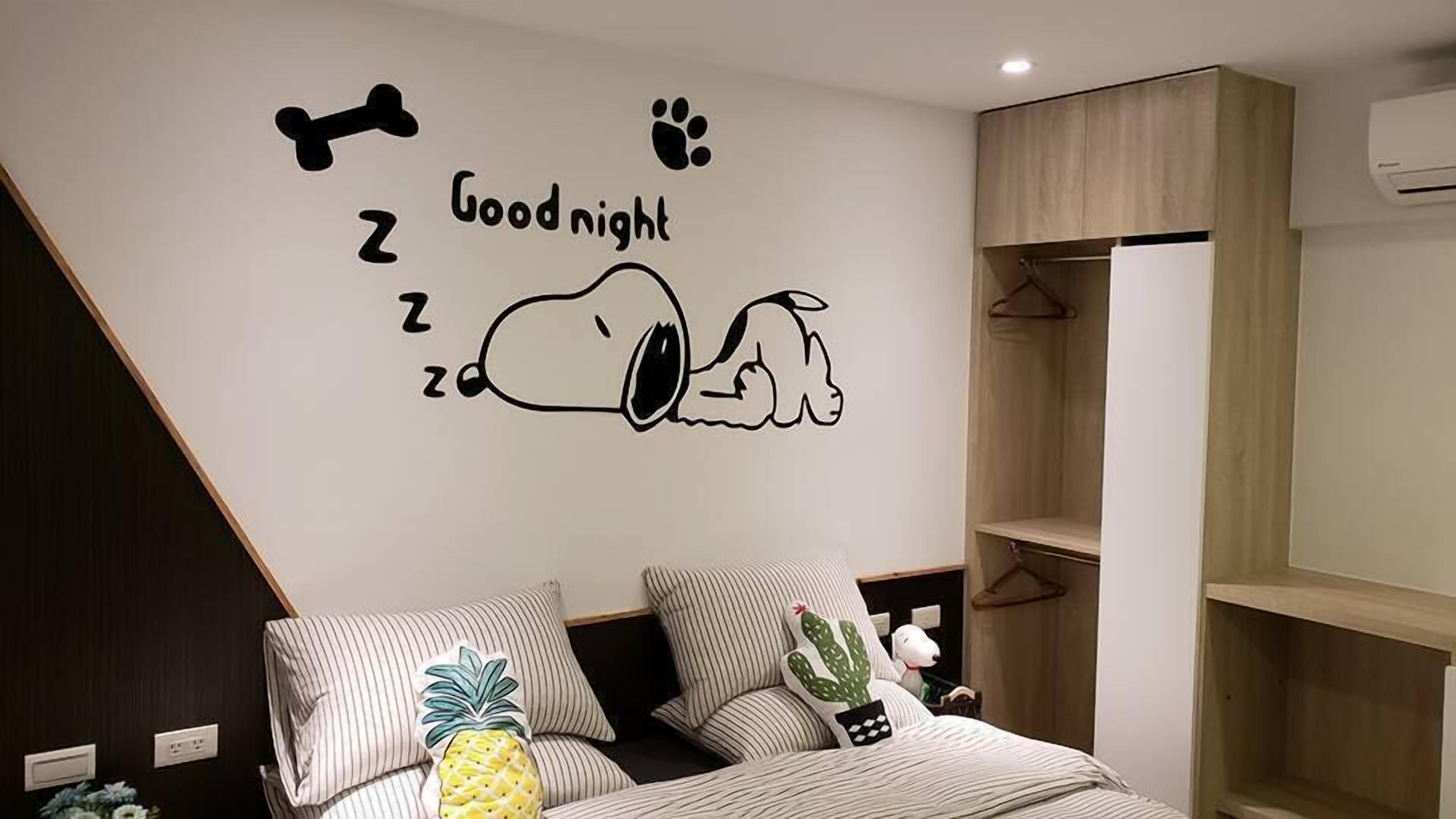 A bedroom with a wall decal of Snoopy sleeping, a bed with striped pillows, and a small cactus decoration.