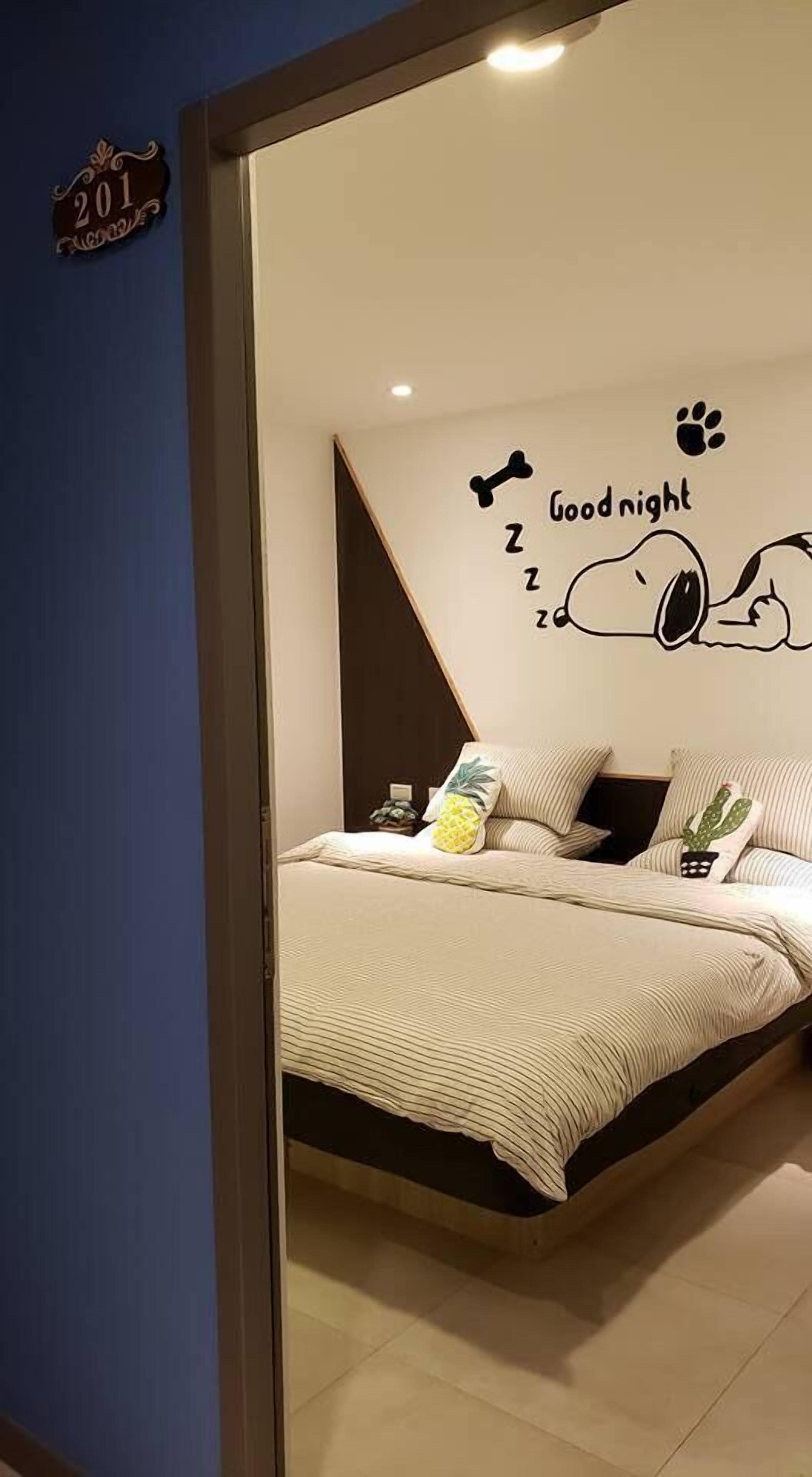 Quarto com cama, decoração de parede com um cão dormindo e uma pequena planta de cacto.