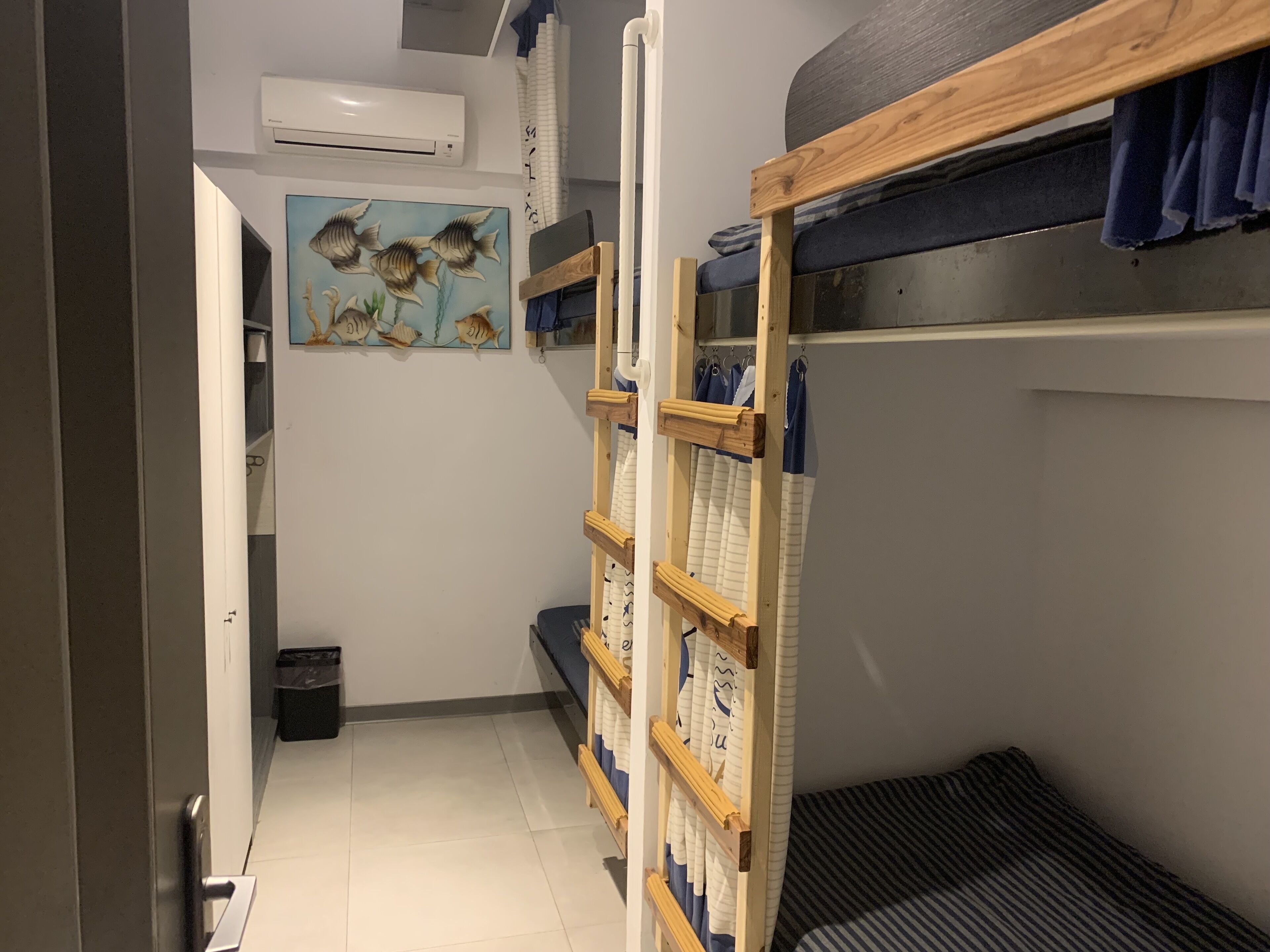 A narrow hallway with bunk beds, a painting of fish, and an air conditioning unit on the wall.