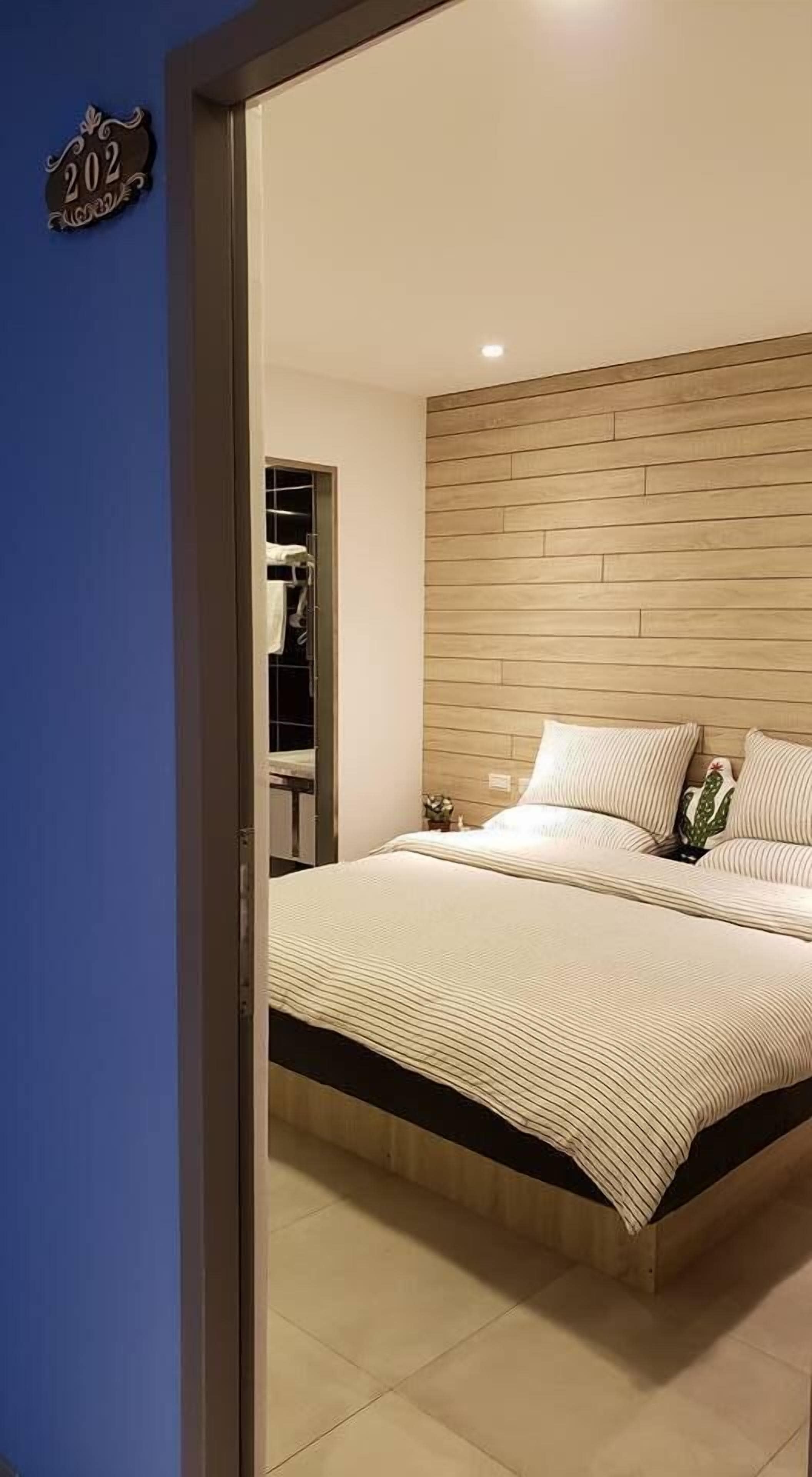A bedroom with a wooden headboard, a bed with white bedding, and a nightstand with a lamp.