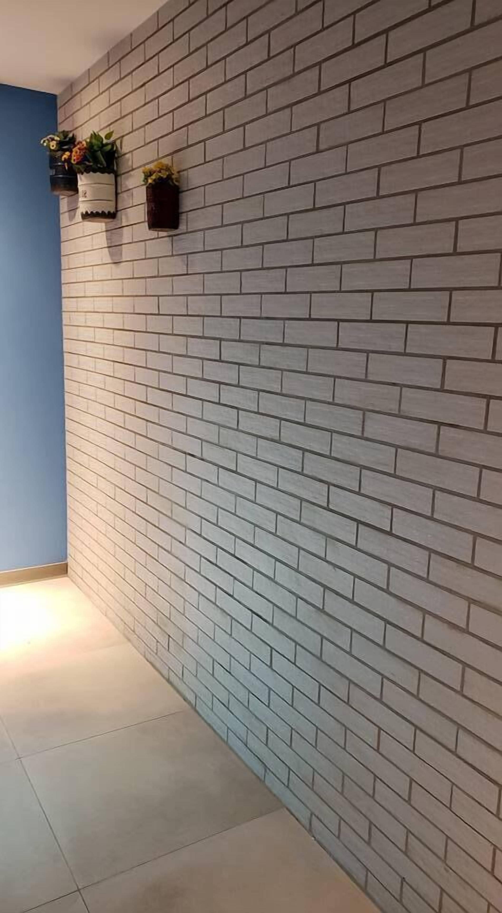 A corner of a room with a white brick wall and a blue accent wall. There are two small black planters with plants on the brick wall.