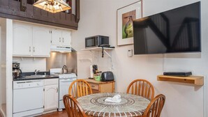Een compacte keuken met witte kasten, een fornuis, een magnetron en een eethoek met een ronde tafel en vier stoelen.