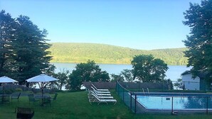 Un jardin avec une piscine, des chaises longues et une vue sur un lac et des collines boisées.