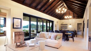 A spacious living area with a white sofa, dining table, and chairs, a wooden cabinet, and a large window offering a mountain view. - Beautiful 4 bedroom Caribbean Villa (Basseterre)
