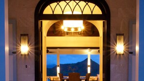 A dining area with a view of mountains, a staircase leading up, and a large arched doorway with lights. - Beautiful 4 bedroom Caribbean Villa (Basseterre)