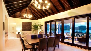A spacious dining area with a large table and chairs, a chandelier, and a view of the mountains through large sliding glass doors. - Beautiful 4 bedroom Caribbean Villa (Basseterre)