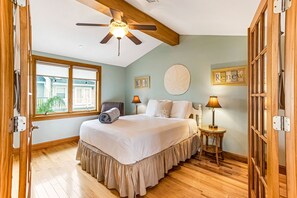 Une chambre avec un grand lit, un ventilateur de plafond, une fenêtre donnant sur un beau paysage et un plancher en bois.