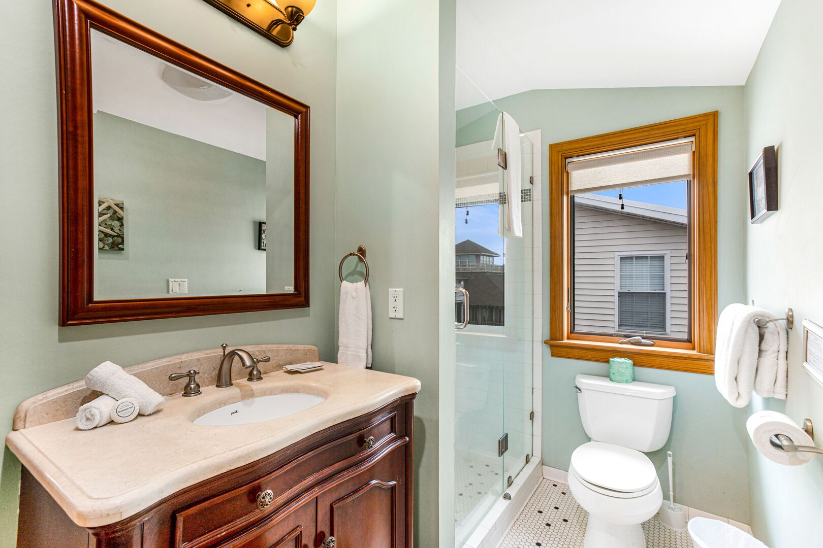 A bathroom with a wooden vanity, a large mirror, a toilet, and a shower area.