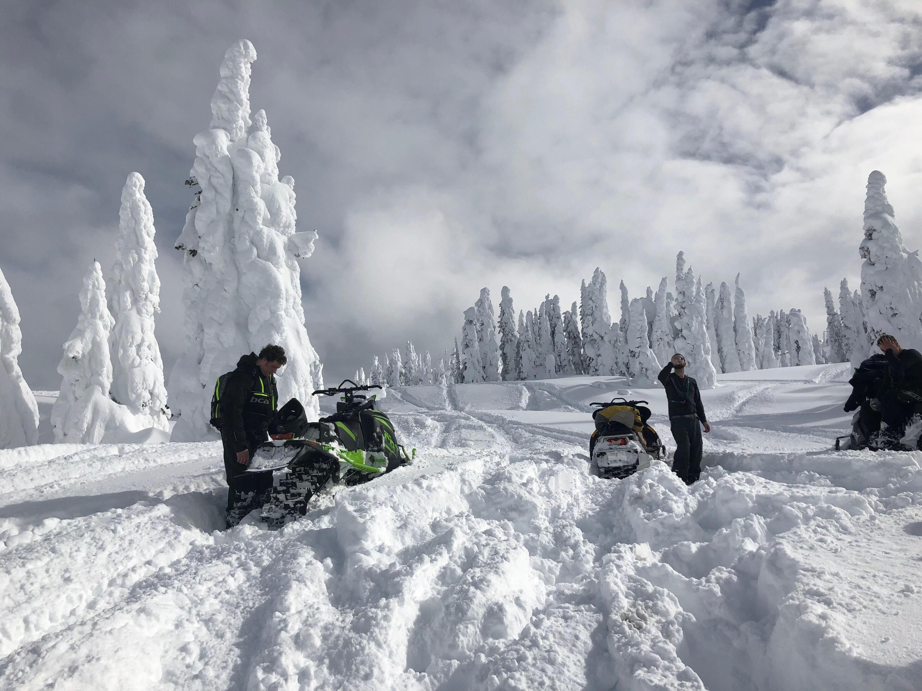 A snow-covered landscape with a snowmobile and a person adjusting it.