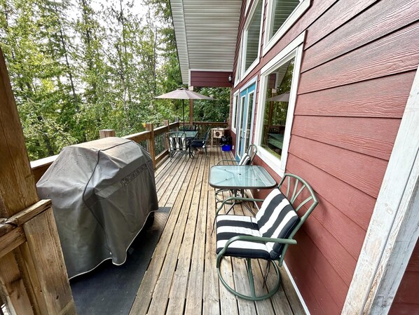 A wooden deck with a covered grill, outdoor furniture, and a view of a forested area.