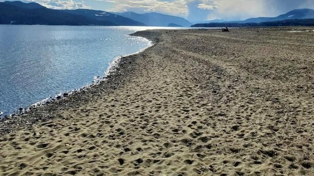 Una playa con cielo despejado y montañas al fondo.