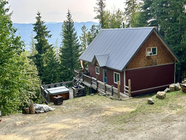 A cabin with a wooden exterior, a metal roof, and a deck with outdoor furniture. - Cozy Cariboo Cabin w/ HOT TUB - Shuswap Vacations and Sledding Accommodation (Anglemont)
