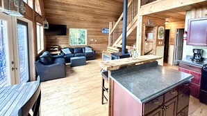 Interior de una cabaña de madera con sala de estar, cocina y una escalera.