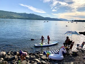 A lakeside scene with people on paddleboards, inflatable floats, and a beach chair area. - Cozy Cariboo Cabin w/ HOT TUB - Shuswap Vacations and Sledding Accommodation (Anglemont)