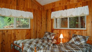 Un dormitorio de cabaña de madera con dos camas, cada una con ropa de cama escocesa y cortinas blancas.
