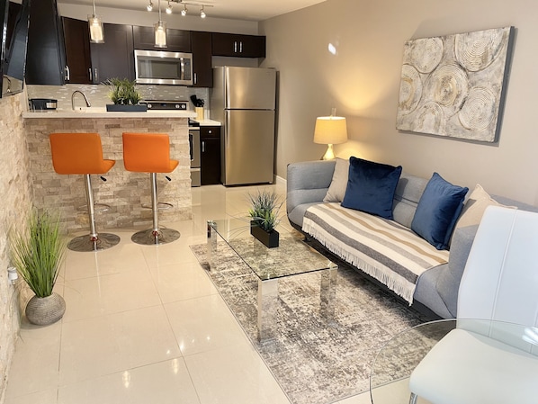 A modern kitchen with a microwave, refrigerator, and bar stools.