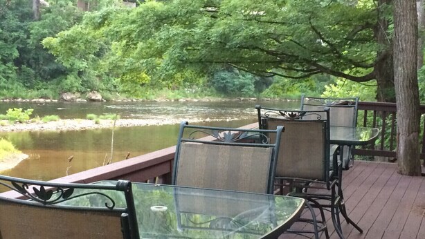 Una terrazza con tavoli e sedie dal piano in vetro, affacciata su un'acqua calma e una vegetazione lussureggiante.