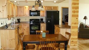 A kitchen with wooden cabinets, a black refrigerator, a microwave, and a dining table with chairs.