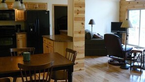 A compact kitchen with a refrigerator, microwave, and wooden cabinets. A dining area with a table and chairs is adjacent to the kitchen.
