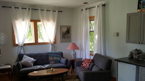 En stue med to sofaer, et lille bord med en vase, en lampe og et køkkenområde med skabe og et køleskab.