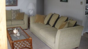 A living room with a beige sofa, a glass coffee table, and two paintings on the walls. - Historic District Ocean Block Lbi Duplex with free tram to the beach (Barnegat Light)