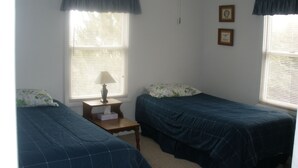 A bedroom with two single beds, a nightstand with a lamp, and two framed pictures on the wall. - Historic District Ocean Block Lbi Duplex with free tram to the beach (Barnegat Light)