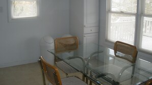 A room with a glass table, four wicker chairs, a white cabinet, and two windows with blinds. - Historic District Ocean Block Lbi Duplex with free tram to the beach (Barnegat Light)