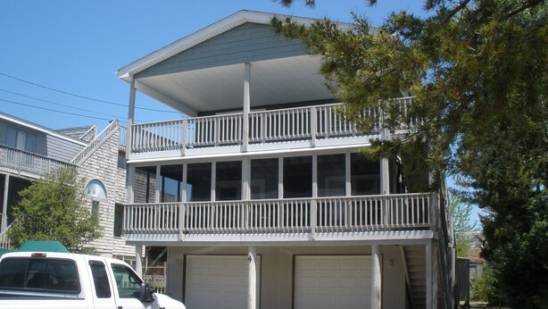 A two-story building with a balcony, a garage, and a parked truck. - Historic District Ocean Block Lbi Duplex with free tram to the beach (Barnegat Light)