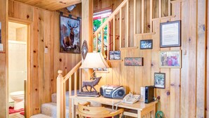 Een houten interieur met een trap, een bureau met een lamp, een stoel, een telefoon en diverse ingelijste foto's.