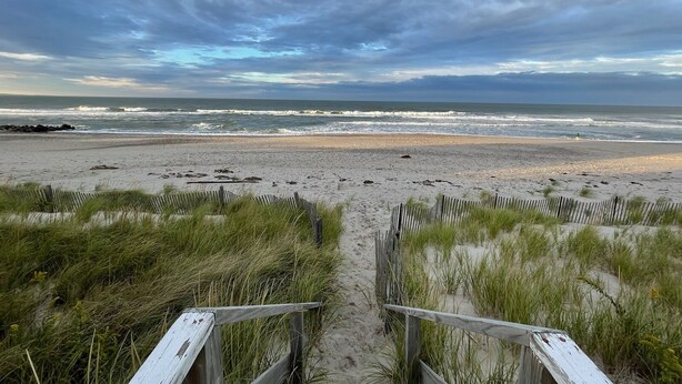 A beach with a wooden pathway leading to the water, surrounded by sand and grass. -  Cozy Cape Cottage on Private Beach with HVAC split AC/Heating system (Sandwich)