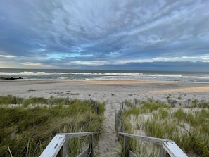 A beach with a wooden pathway leading to the water, surrounded by sand and grass.
