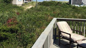 A wooden deck with a single chair, surrounded by dense greenery and a clear sky. -  Cozy Cape Cottage on Private Beach with HVAC split AC/Heating system (Sandwich)