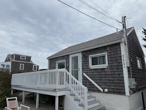 A residential house with a front porch, a staircase leading to the entrance, and a visible electrical box on the side. - Cozy Cape Cottage on Private Beach with HVAC split AC/Heating system (Sandwich)