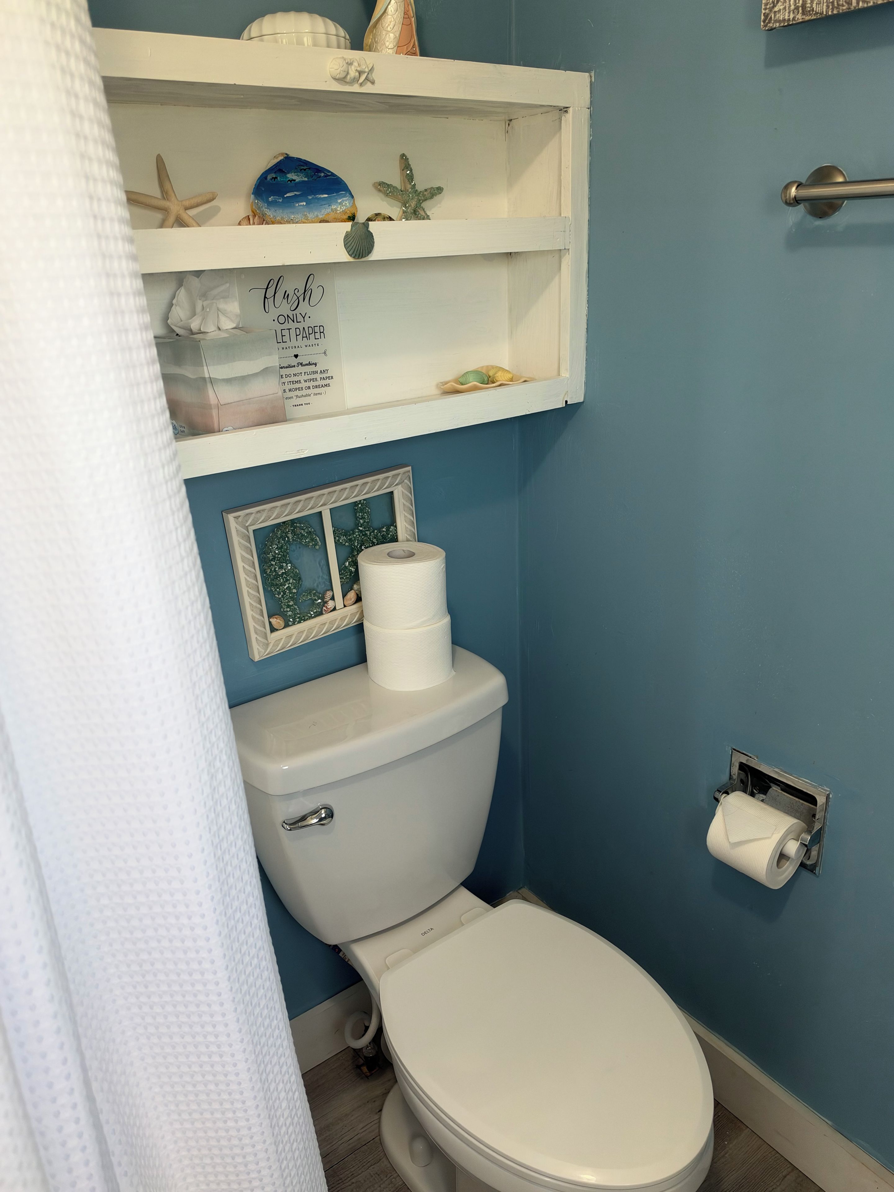 A bathroom with a toilet, a shelf with decorative items, and a roll of toilet paper.