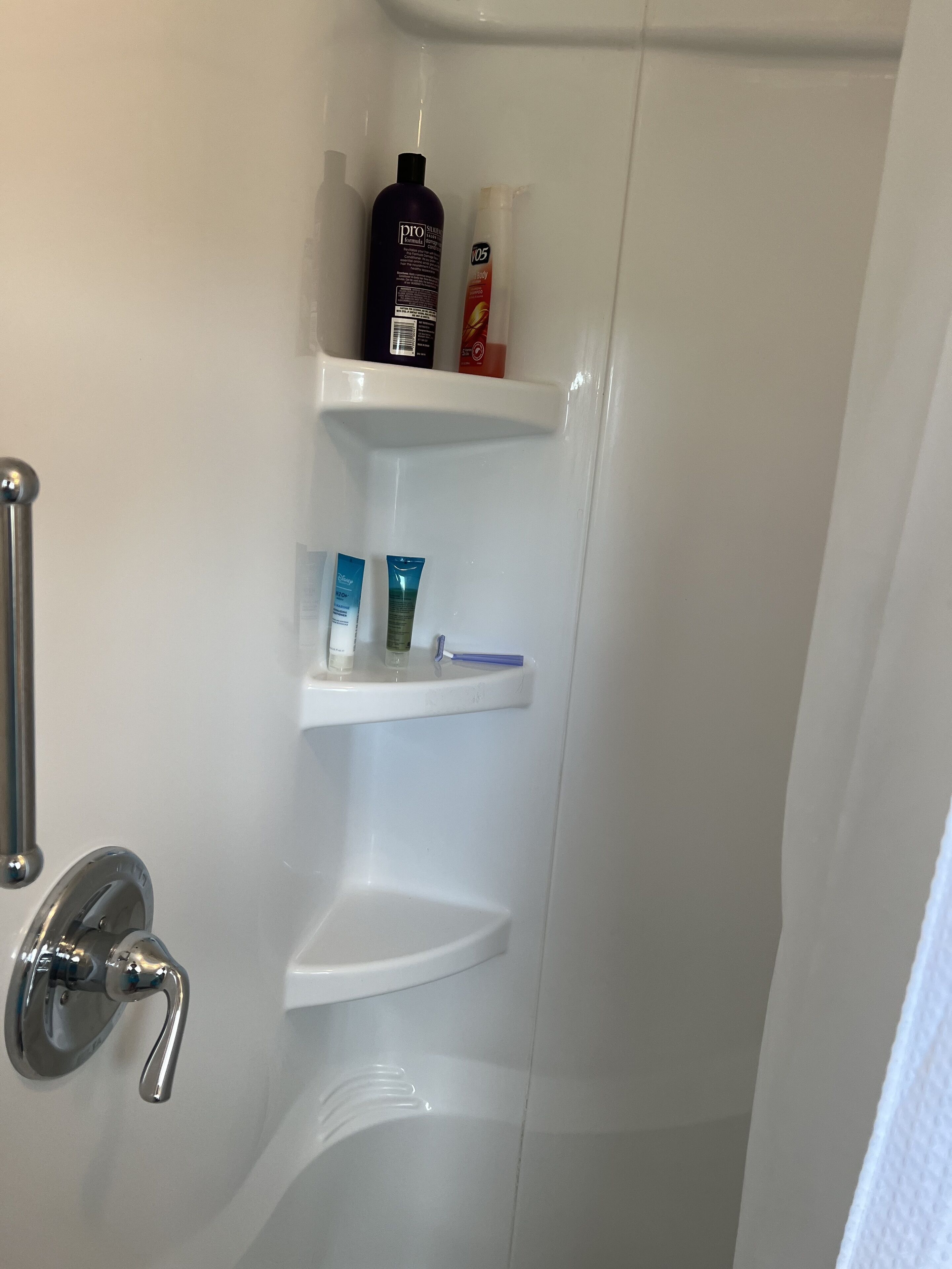 Une salle de bain avec une douche, des toilettes et un lavabo. On y trouve des étagères avec des produits de toilette.