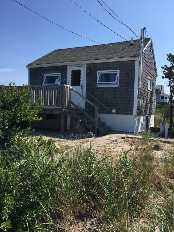A two-story house with a wooden deck, a front door, and a staircase leading to the entrance.