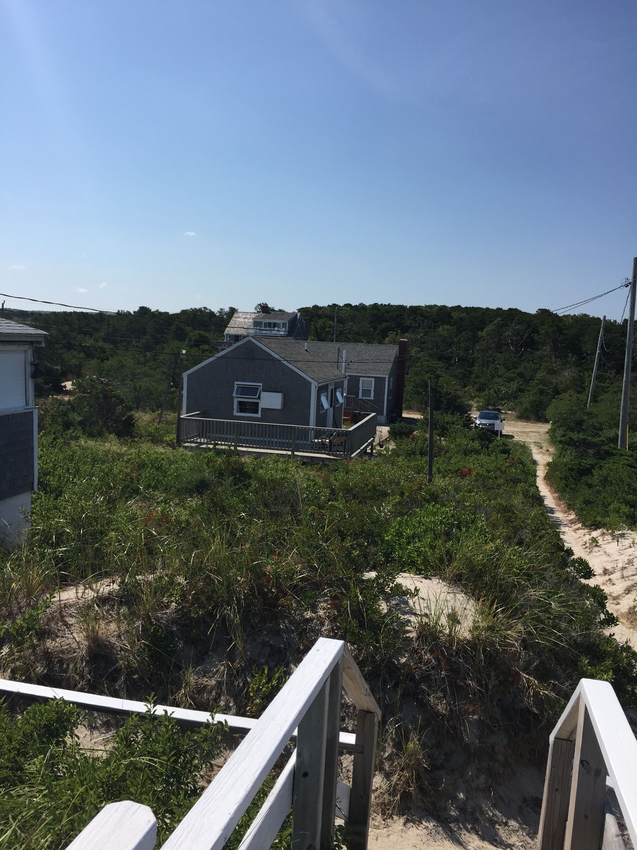 A beach house with a wooden deck and a sandy path leading to it.