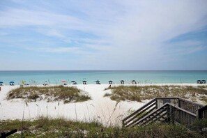 A beach with a wooden staircase leading down to the sand, a row of beach umbrellas, and a clear view of the ocean. - Beautiful Ground Floor Unit! (Miramar Beach)