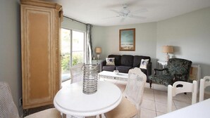 A living room with a white table, two white chairs, a dark sofa, a patterned armchair, and a ceiling fan.