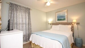 A bedroom with a bed, a ceiling fan, a nightstand, a lamp, and a picture on the wall.