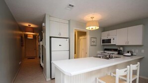 A kitchen with white cabinets, a built-in microwave, a refrigerator, and a small island with two chairs.