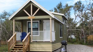 Une petite cabane avec une véranda, une chaise bleue et un barbecue à l’extérieur.