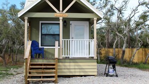 Une petite cabane en bois avec une véranda, une chaise bleue et un barbecue.