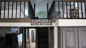 Une chambre de style « loft », avec une pancarte indiquant « Quartiers du capitaine » au-dessus d’un escalier.