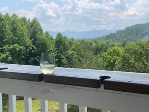 A glass of white wine on a wooden deck railing with a view of a forested landscape and mountains in the distance. - Mountain View ranch w/ sauna, 1ac fence & firepit. (Candler)