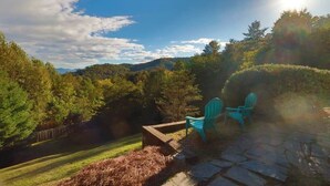 An outdoor patio with stone flooring and two green chairs, surrounded by a lush garden and a view of distant hills. - Mountain View ranch w/ sauna, 1ac fence & firepit. (Candler)