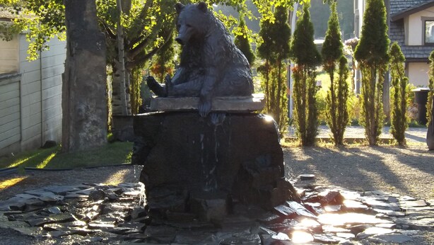 En stenstøbt bjørn statue sidder på en klippe med en å der løber omkring den.