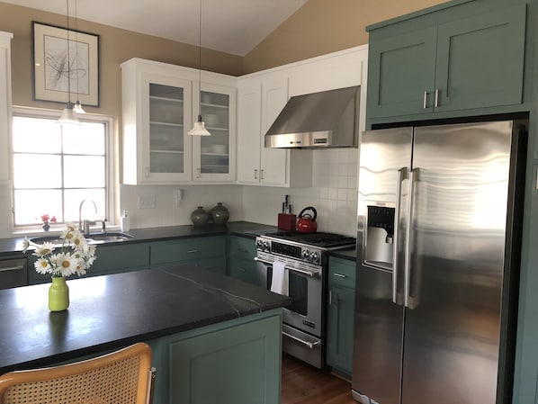 A kitchen with teal cabinets, a stainless steel refrigerator, a stove, and a sink.